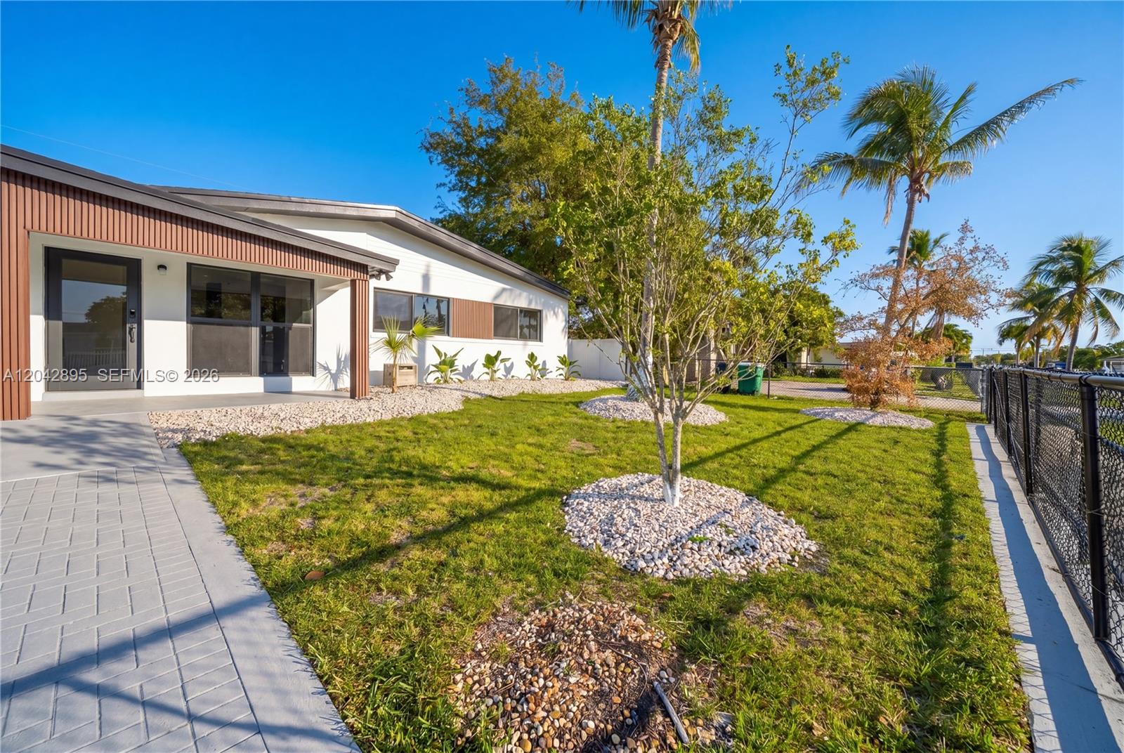 A white house exterior features a paved walkway, rock-mulched landscaping, and several palm trees — 12471 SW 190th Ter, Miami FL 33177, MIAMI, FL