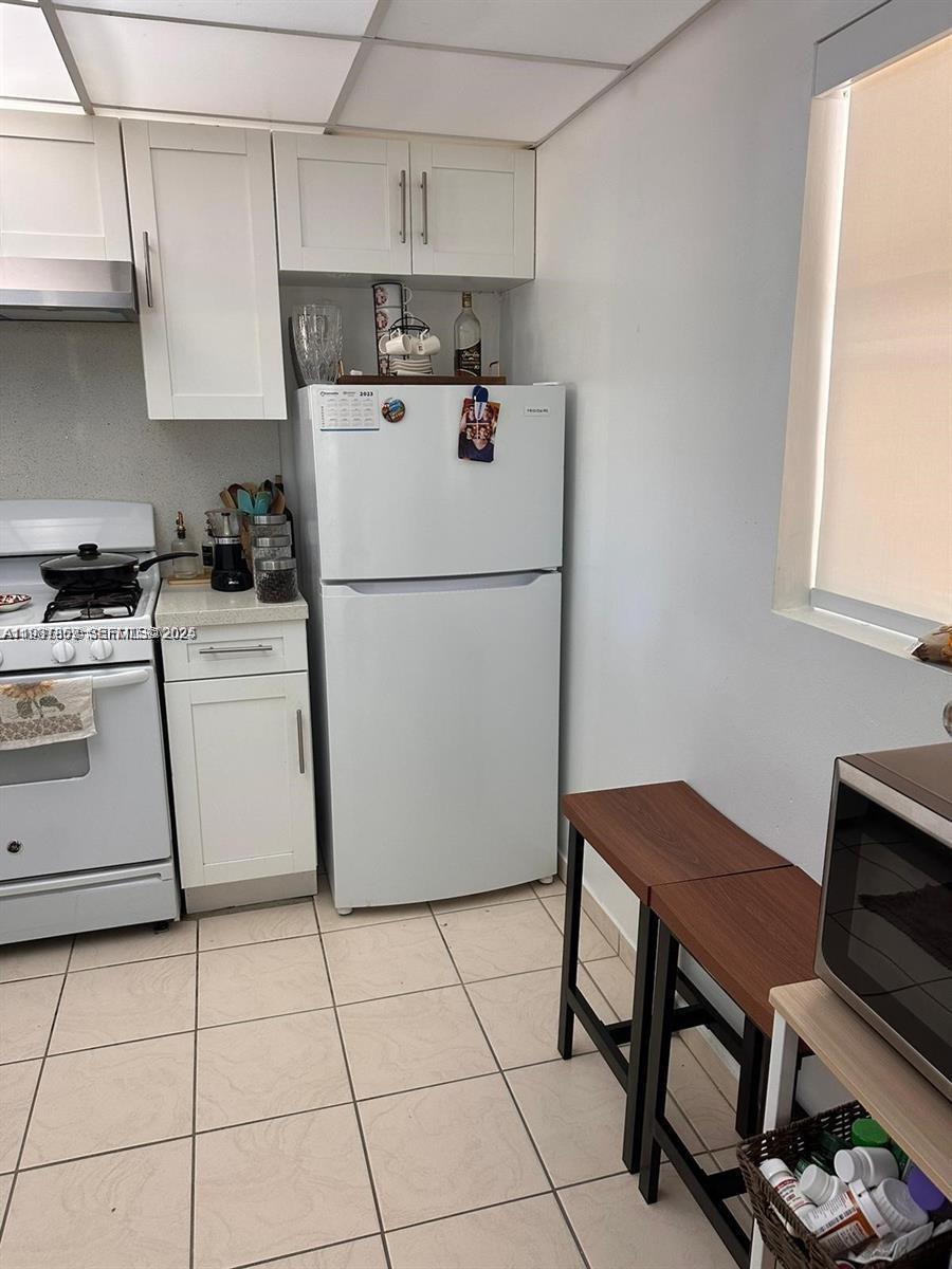 A small kitchen features white cabinets, a white refrigerator, a gas stove, and tile flooring — 18101 NW 68th Ave # C202, Hialeah FL 33015, HIALEAH, FL
