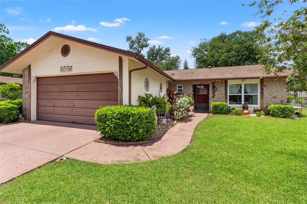 A single-story house with a brown garage door, stone accents, and a front lawn — 10541 GREEN MEADOW LANE, PORT RICHEY, FL