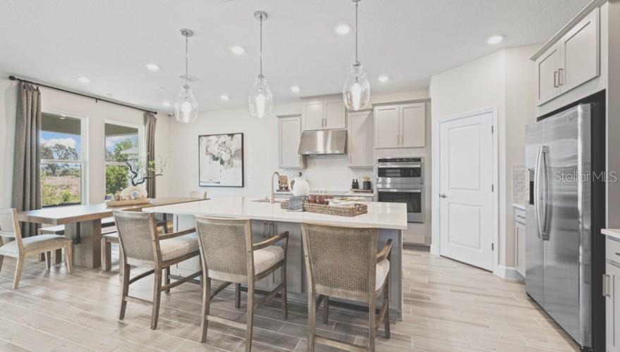 A modern kitchen features a large island with bar stools, stainless appliances, and light cabinetry — 3116 LUMBER FALLS DRIVE, PLANT CITY, FL