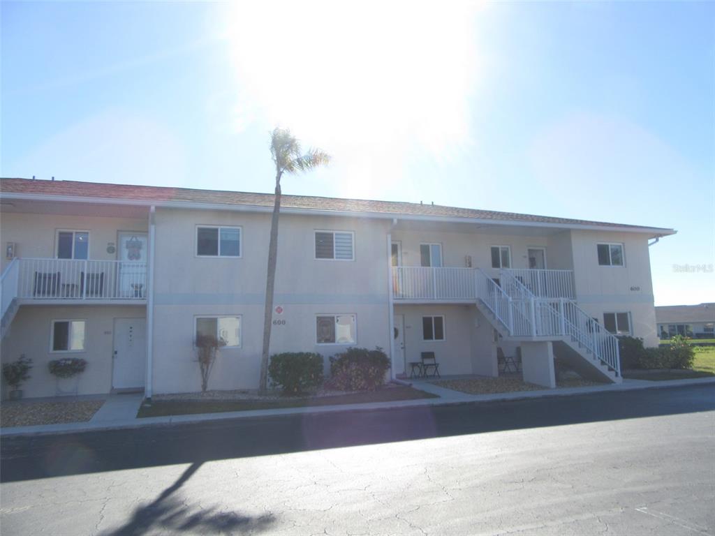 A two-story apartment building with white stucco walls, a palm tree, and exterior staircases — 12538 SW KINGSWAY CIRCLE UNIT 607, LAKE SUZY, FL