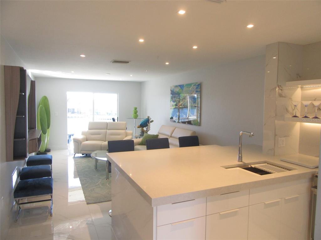 A modern kitchen island with a sink overlooks a living area with white leather furniture — 12538 SW KINGSWAY CIRCLE UNIT 607, LAKE SUZY, FL