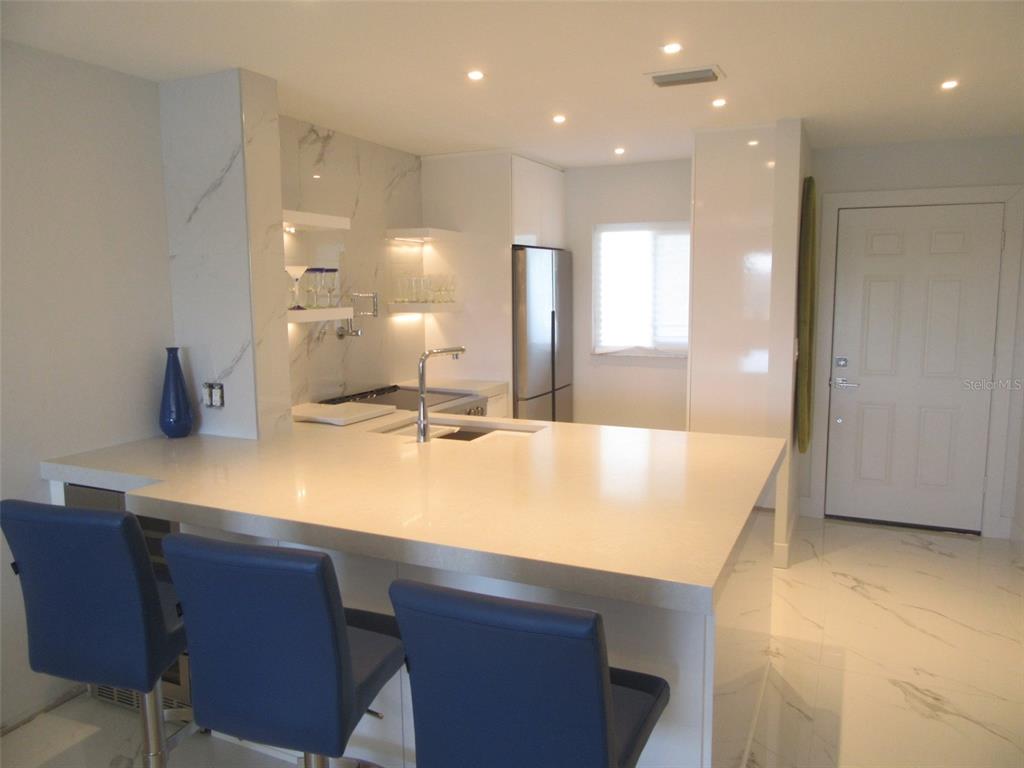 A modern kitchen features white quartz countertops, blue bar stools, and marble-style flooring — 12538 SW KINGSWAY CIRCLE UNIT 607, LAKE SUZY, FL
