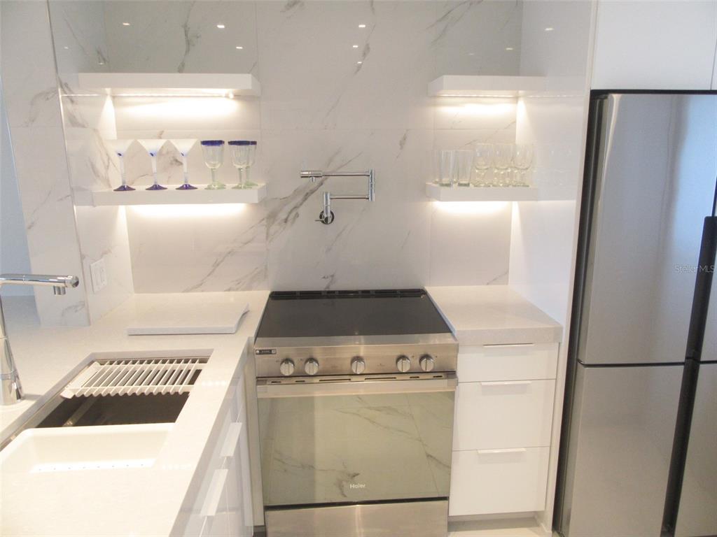 A modern kitchen features white marble walls, floating shelves, a stainless steel stove, and refrigerator — 12538 SW KINGSWAY CIRCLE UNIT 607, LAKE SUZY, FL