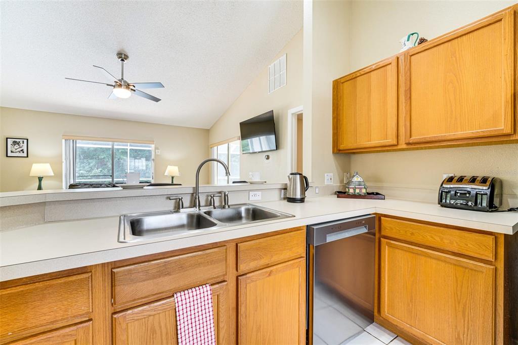 A kitchen features wood cabinets, a double sink, a dishwasher, and a view into the living room — 630 THOUSAND OAKS BOULEVARD, DAVENPORT, FL