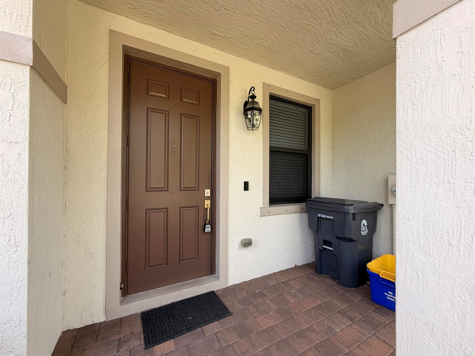 A brown front door and a window are located on a covered brick porch — 6145 Bangalow Drive, Lake Worth FL 33463, LAKE WORTH, FL