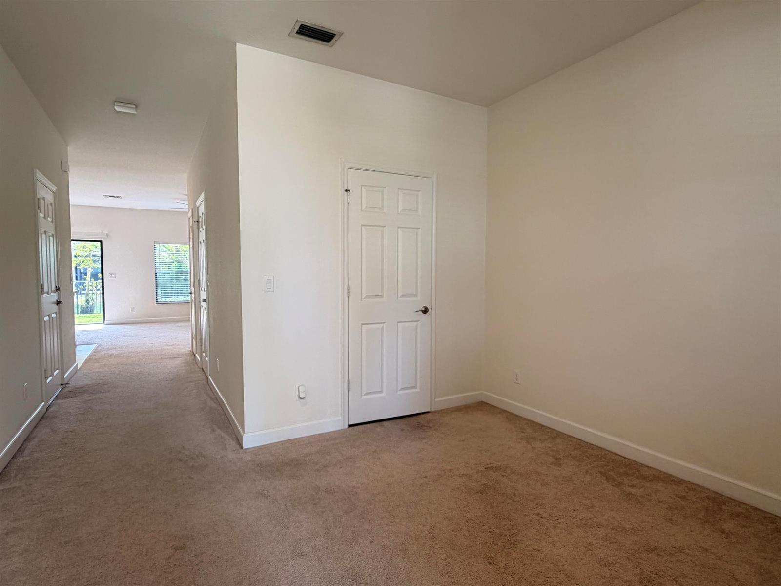 A carpeted room with a white door leads into a hallway with a glass door — 6145 Bangalow Drive, Lake Worth FL 33463, LAKE WORTH, FL