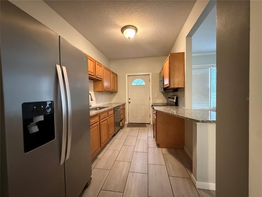 A galley kitchen features wood cabinets, granite countertops, stainless steel appliances, and light tile flooring — 325 W JEAN STREET, TAMPA, FL