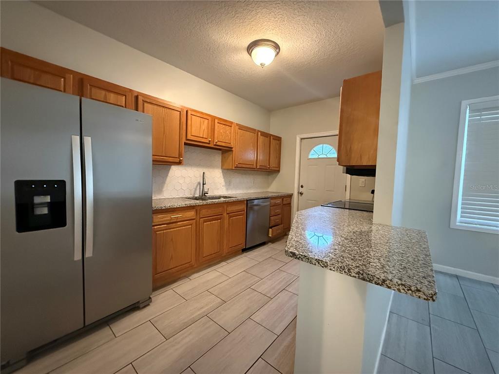 A kitchen features wood cabinets, granite countertops, stainless steel appliances, and light-colored tile flooring — 325 W JEAN STREET, TAMPA, FL