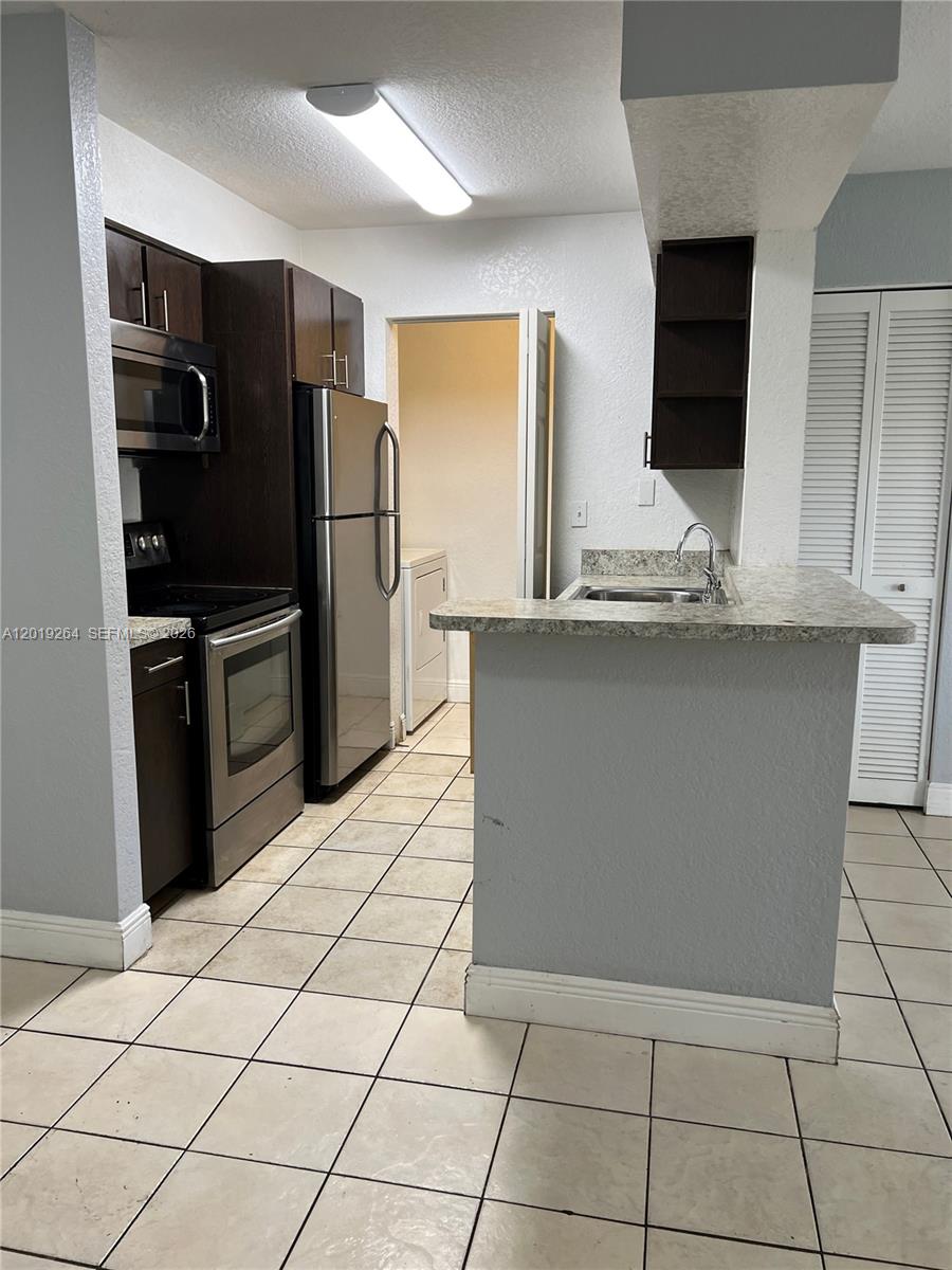 This kitchen features dark wood cabinets, stainless steel appliances, and a tiled floor — 1237 SW 46th Ave # 801, Pompano Beach FL 33069, POMPANO BEACH, FL