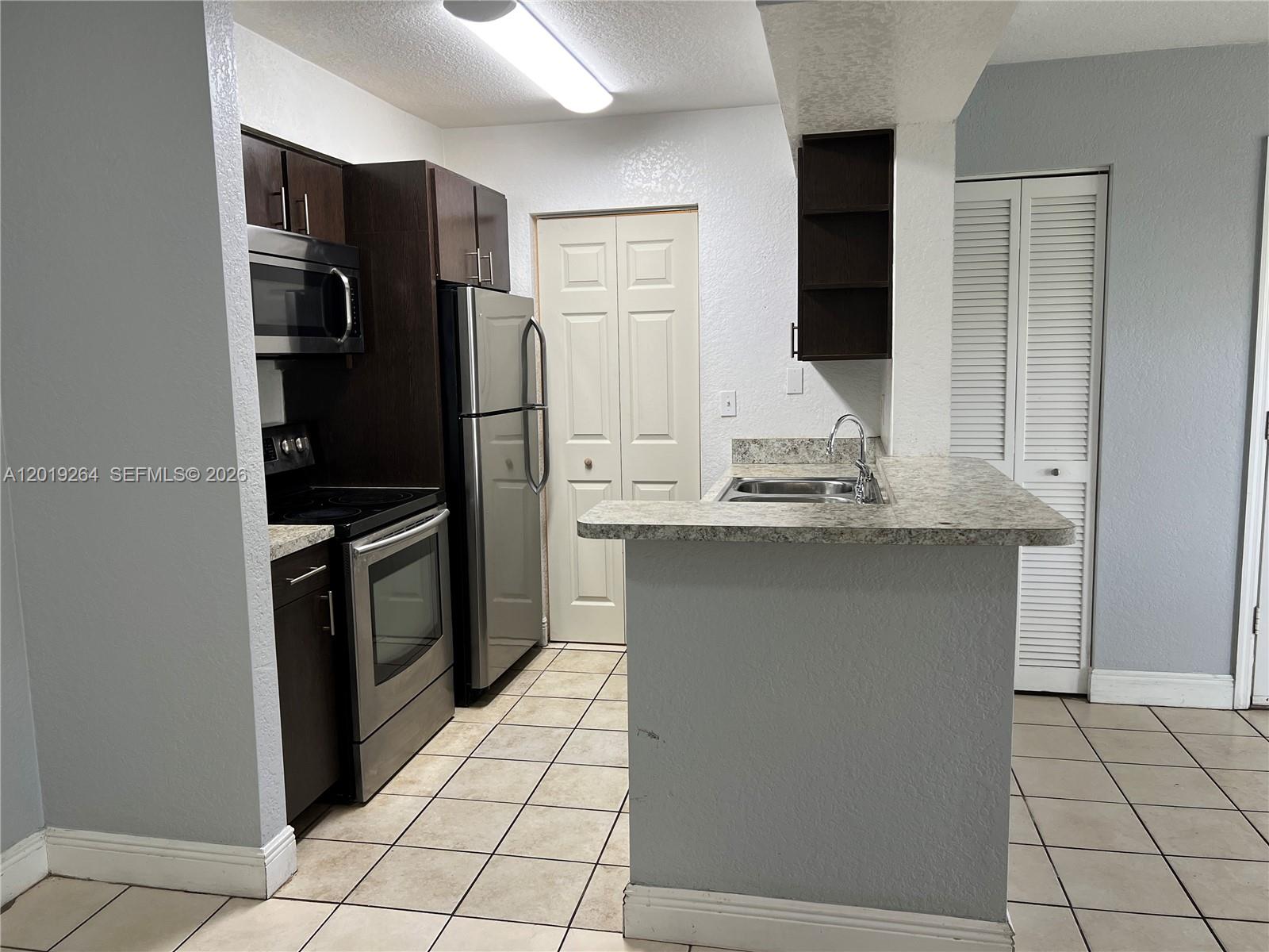 A kitchen features dark wood cabinets, stainless steel appliances, and a granite-topped breakfast bar — 1237 SW 46th Ave # 801, Pompano Beach FL 33069, POMPANO BEACH, FL
