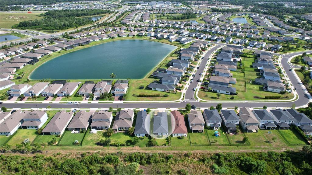 An aerial view shows a suburban neighborhood with houses surrounding a large central lake — 11636 LITTLE RIVER WAY, PARRISH, FL