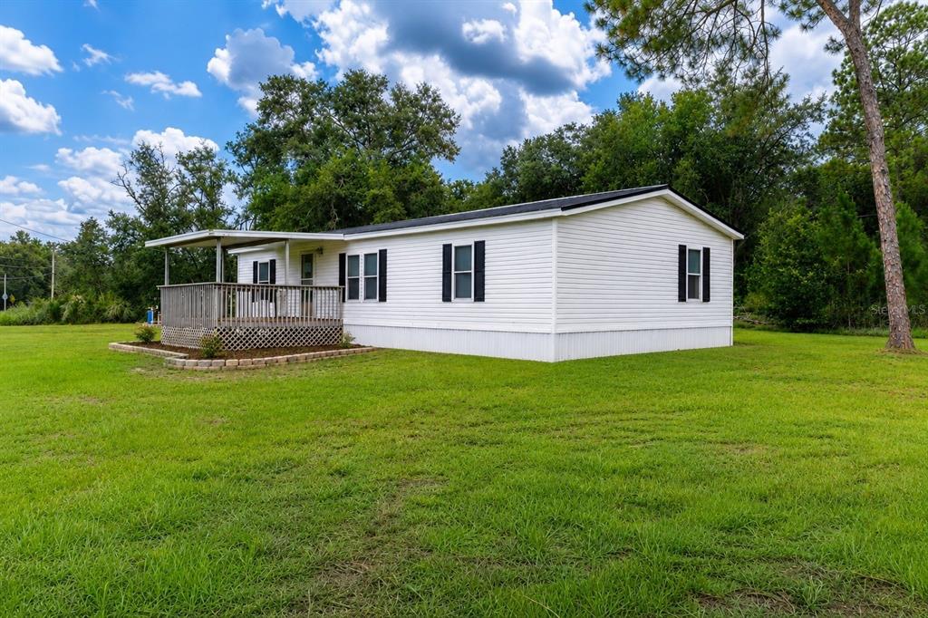 A white mobile home with a wooden deck sits on a large grassy lot — 2140 TRAILSWOOD PATH, LAKELAND, FL