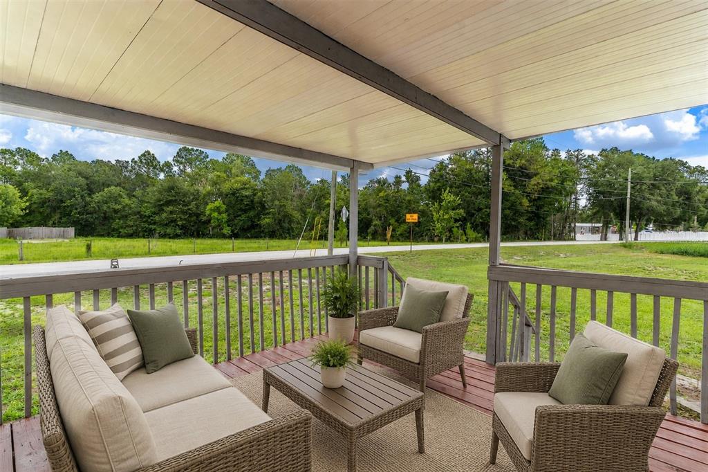A covered wooden deck features wicker patio furniture overlooking a grassy field and trees — 2140 TRAILSWOOD PATH, LAKELAND, FL