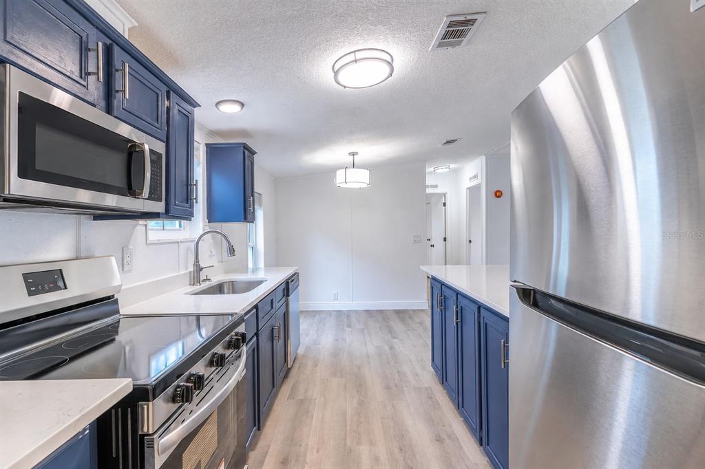 A kitchen features blue cabinets, stainless steel appliances, white countertops, and light wood-look flooring — 2140 TRAILSWOOD PATH, LAKELAND, FL