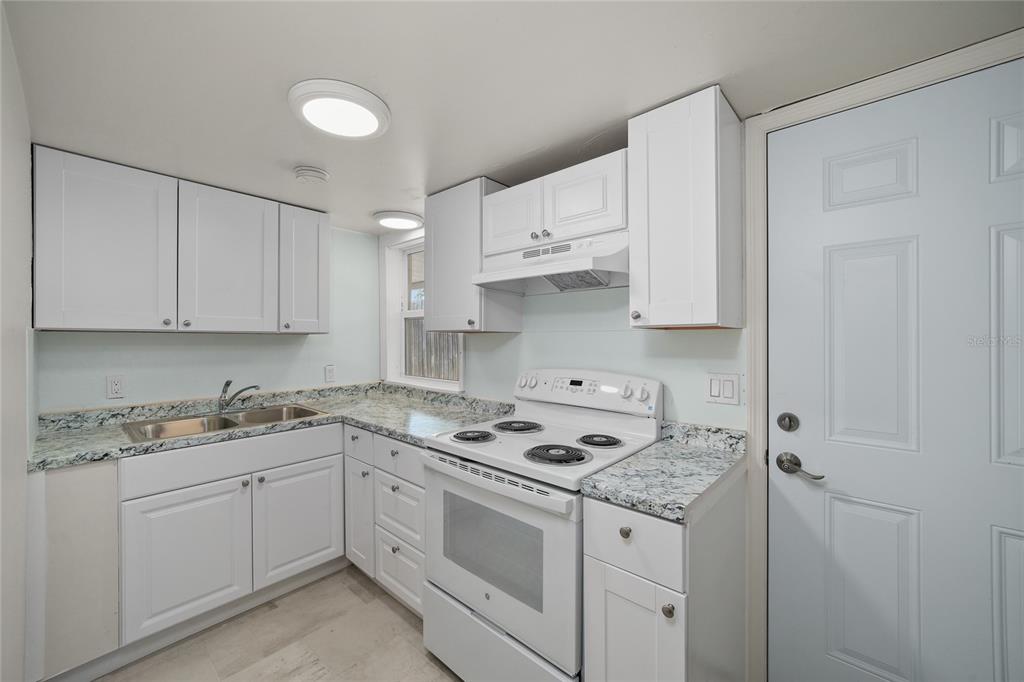 A kitchen features white cabinets, granite countertops, a white stove, and a white exterior door — 4615 N HESPERIDES STREET, TAMPA, FL