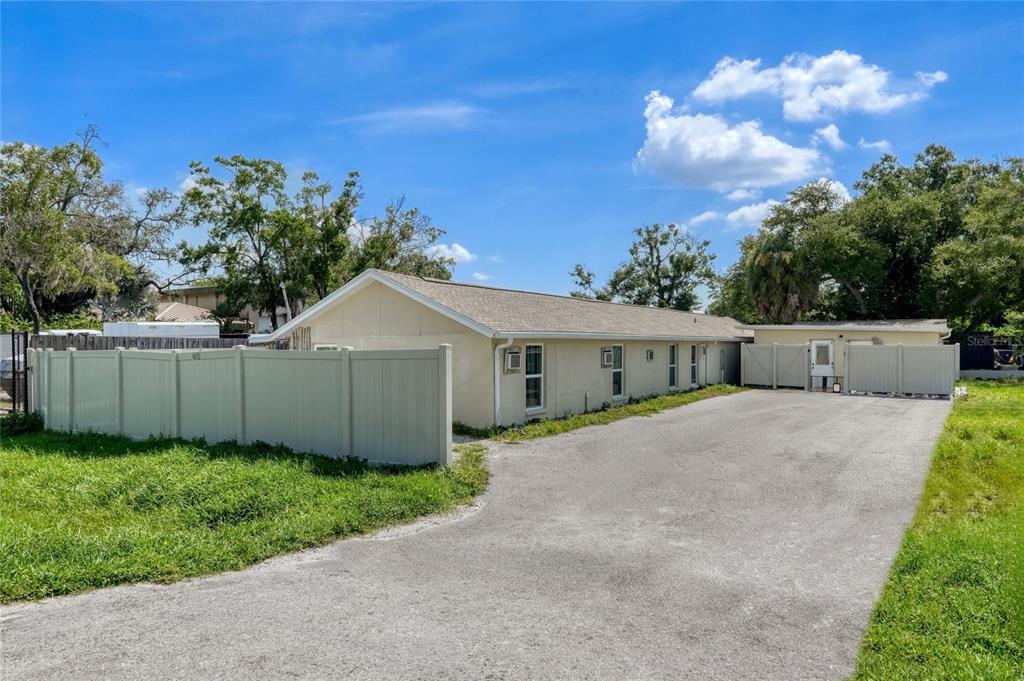 A long, single-story house with light-colored siding sits beside a paved driveway and vinyl fence — 4615 N HESPERIDES STREET, TAMPA, FL