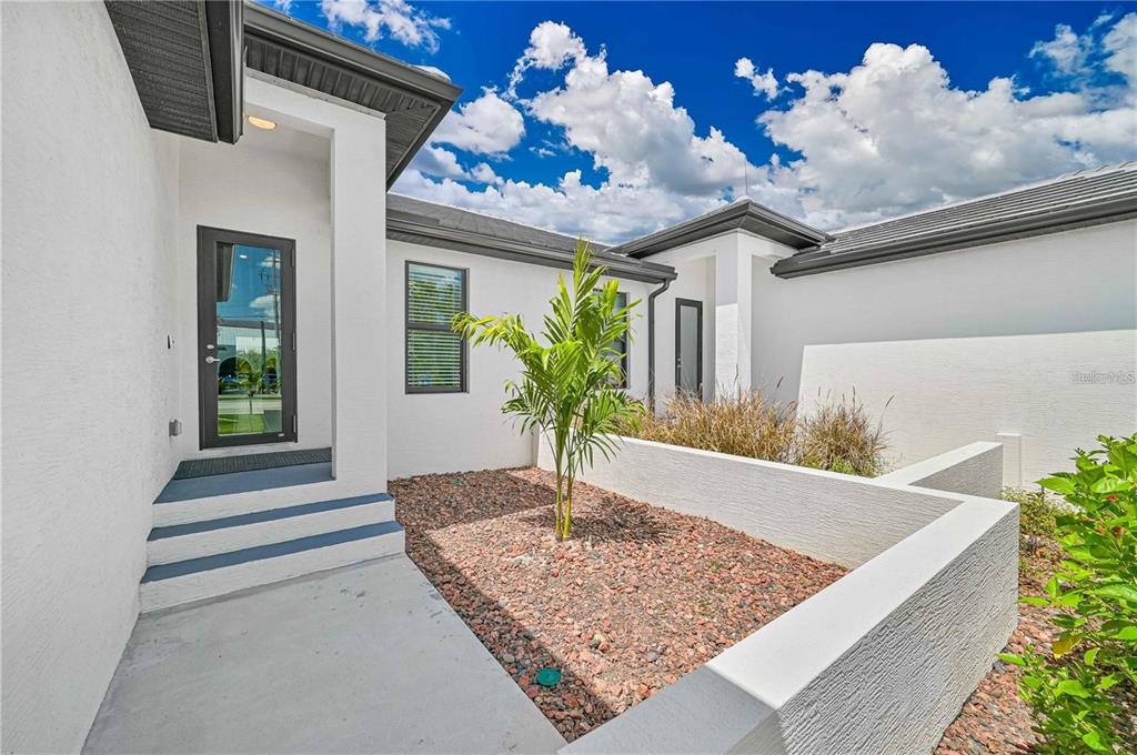 The exterior of a modern home features a white stucco facade, a palm tree, and steps — 180 MADRID BOULEVARD, PUNTA GORDA, FL