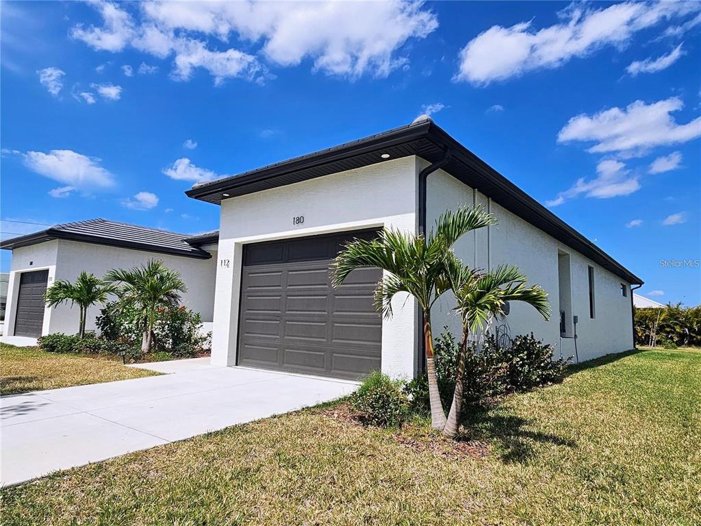 A white house with a dark garage door and palm trees under a blue sky — 180 MADRID BOULEVARD, PUNTA GORDA, FL