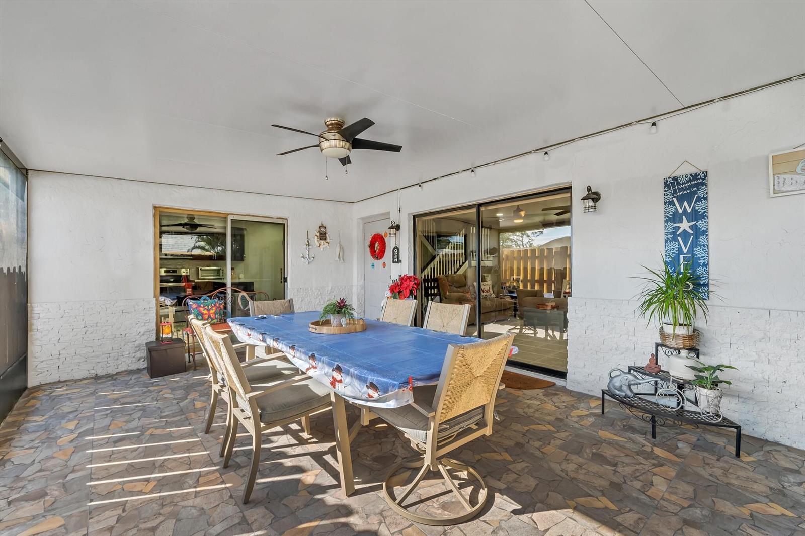 A covered patio features a dining table, stone-patterned flooring, and sliding glass doors — 747 NW 30th Avenue # D, Delray Beach FL 33445, DELRAY BEACH, FL