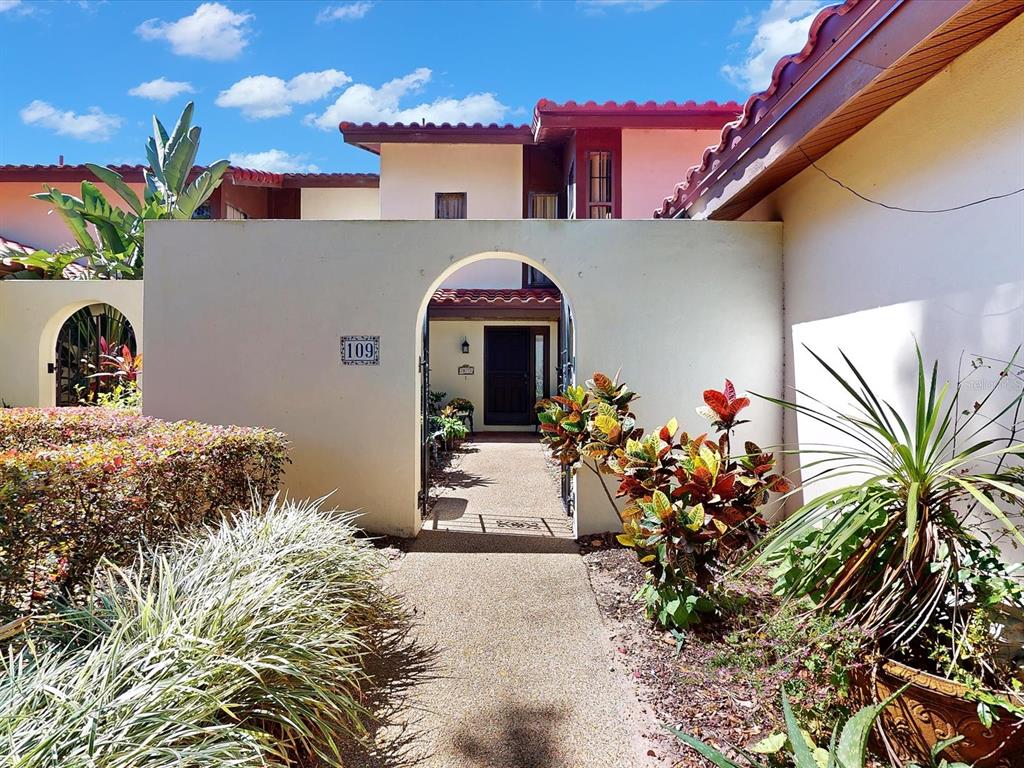 A walkway leads through an arched gate to the entrance of a stucco home — 109 COVENTRY LANE, HAINES CITY, FL