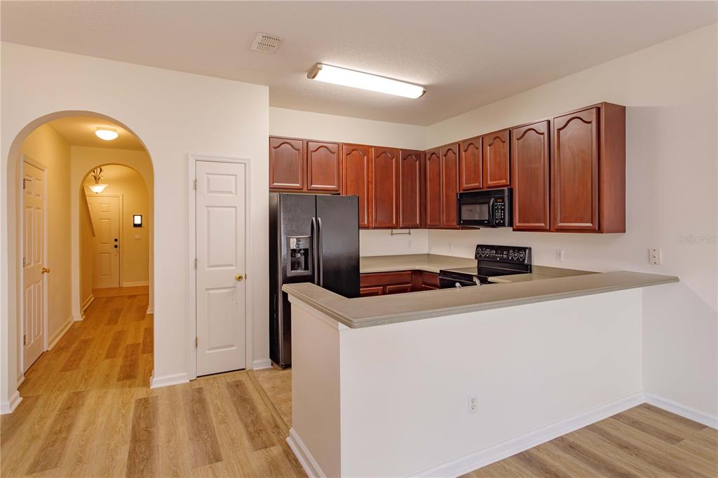 A kitchen with wood cabinets, black appliances, and a breakfast bar overlooks a hallway — 16460 CEDAR CREST DRIVE, ORLANDO, FL
