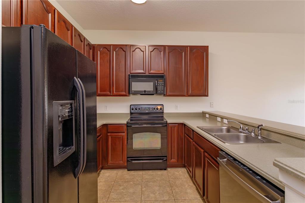 A kitchen features dark wood cabinets, black appliances, a double sink, and tan countertops — 16460 CEDAR CREST DRIVE, ORLANDO, FL