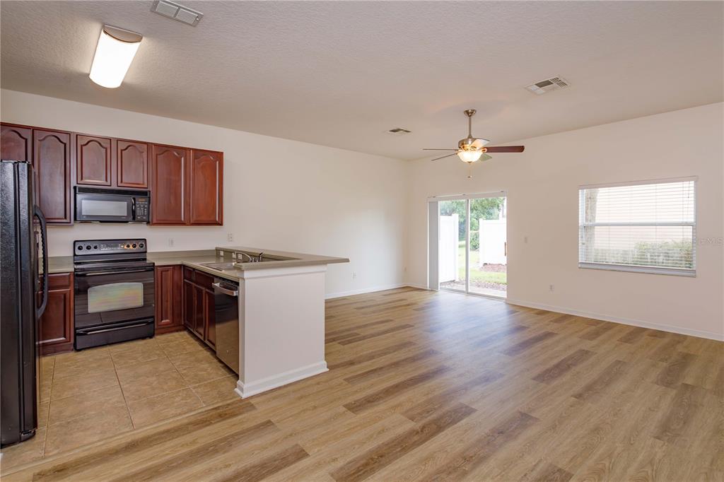 A kitchen with wood cabinets and tile flooring opens into a living area with wood-look floors — 16460 CEDAR CREST DRIVE, ORLANDO, FL