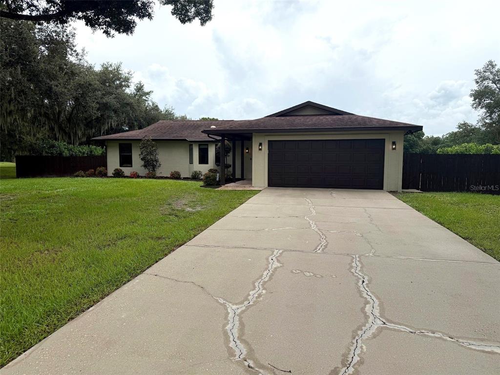 A single-story house with a brown roof, beige exterior, and a cracked concrete driveway — 1003 134TH STREET E, BRADENTON, FL