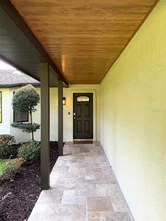 A covered entryway features a stone-tiled walkway, a dark front door, and a wood-paneled ceiling — 1003 134TH STREET E, BRADENTON, FL