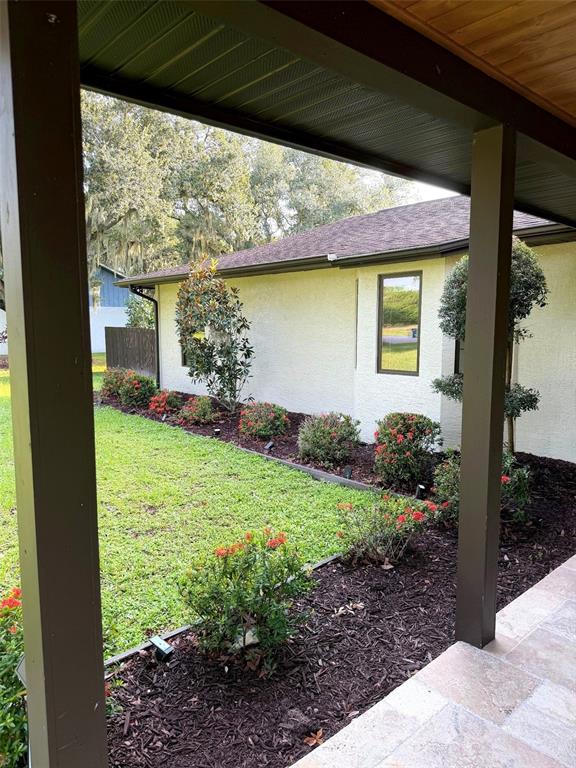 A view from a covered porch looking out at a landscaped yard and house exterior — 1003 134TH STREET E, BRADENTON, FL