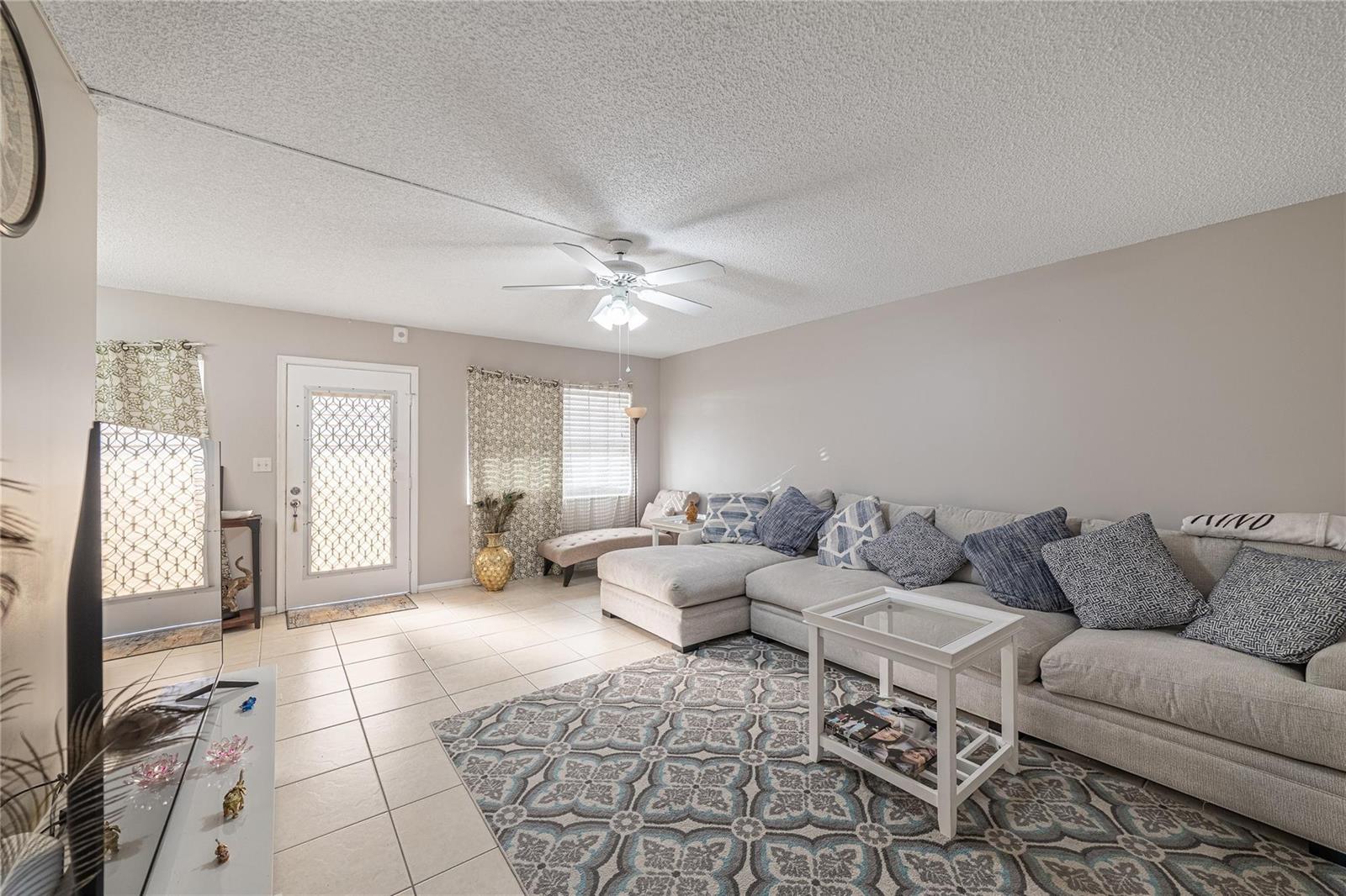 A living room features a large sectional sofa, a patterned area rug, and tile flooring — 1902 Bermuda Circle, Coconut Creek FL 33066, COCONUT CREEK, FL