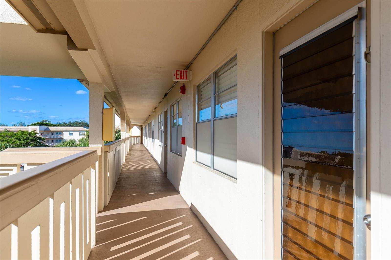 An outdoor apartment building walkway with a railing, windows, and an exit sign — 1902 Bermuda Circle, Coconut Creek FL 33066, COCONUT CREEK, FL