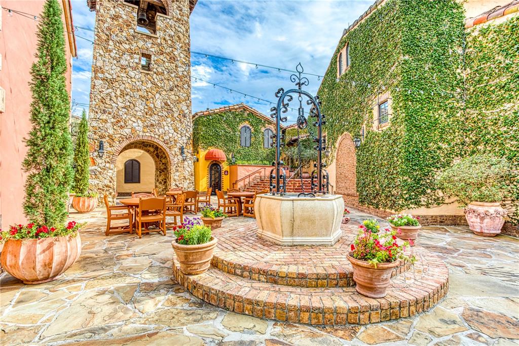 A stone courtyard features a central well, outdoor dining tables, and ivy-covered building walls — 16241 RAVENNA COURT, BELLA COLLINA, FL