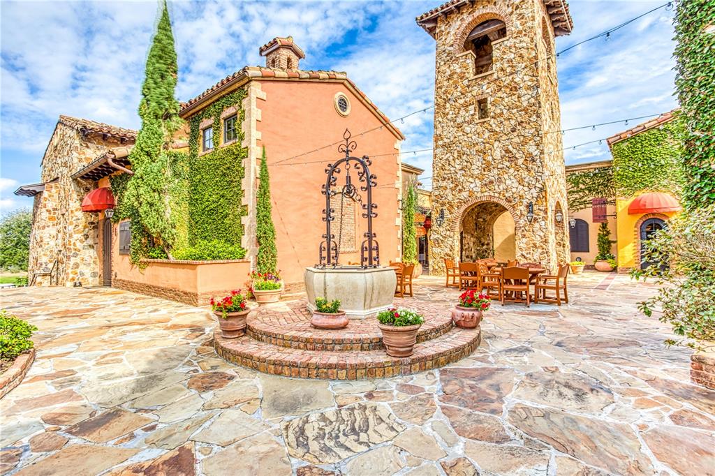 A stone courtyard features a central wishing well, outdoor seating, and Mediterranean-style buildings — 16241 RAVENNA COURT, BELLA COLLINA, FL