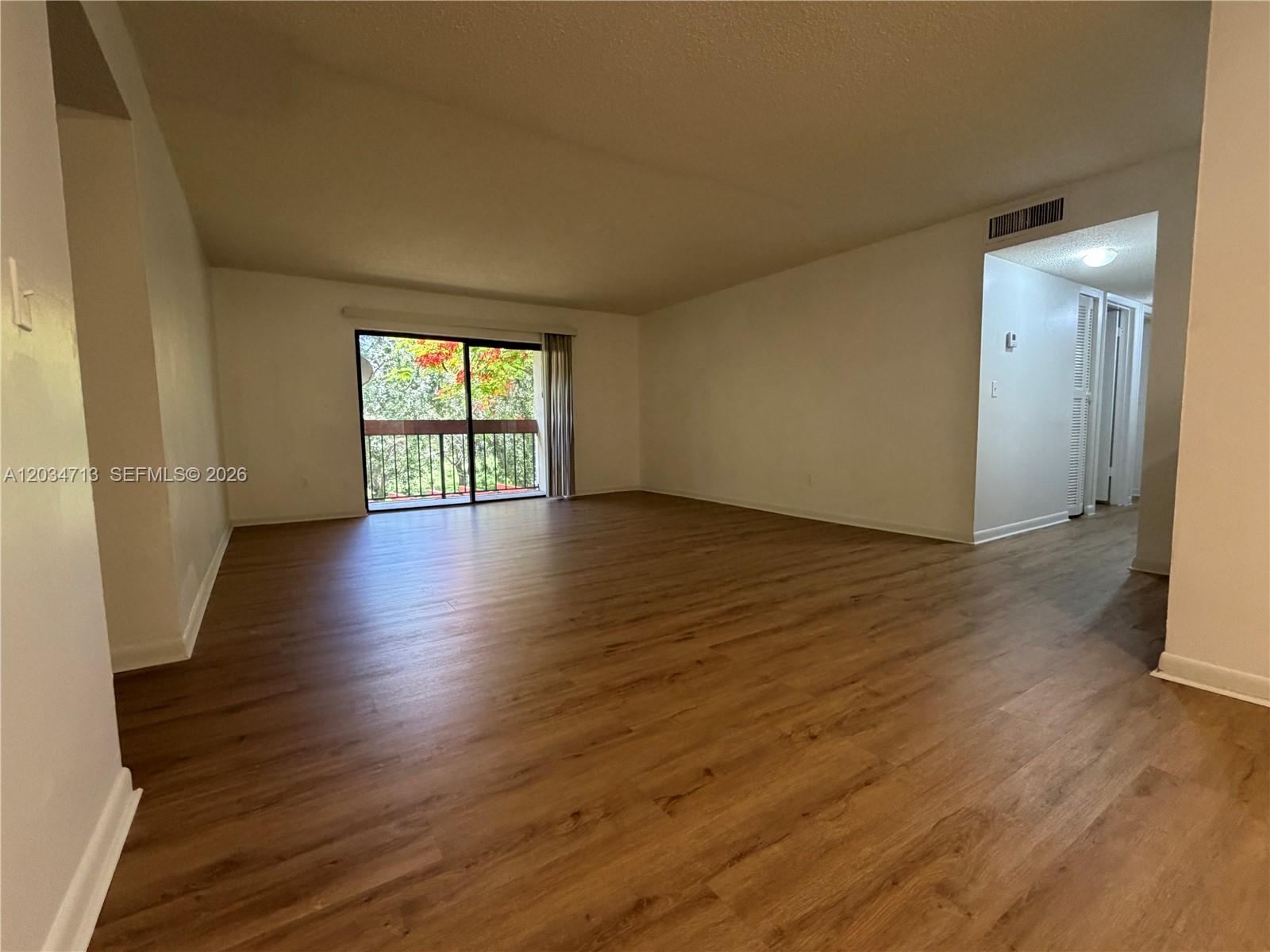 An empty living room features wood-look flooring, white walls, and a sliding glass balcony door — MIAMI, FL