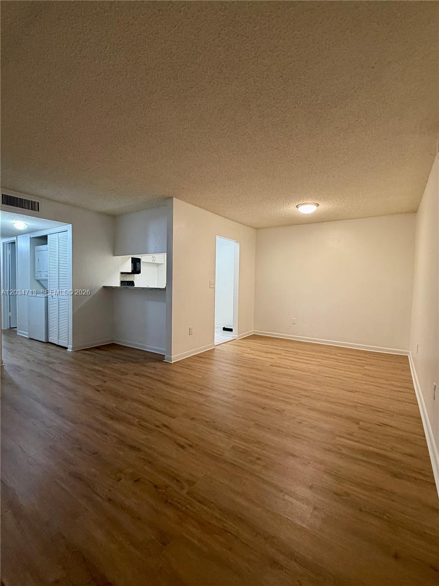 An empty living room features light wood-look flooring, white walls, and an adjacent kitchen area — MIAMI, FL