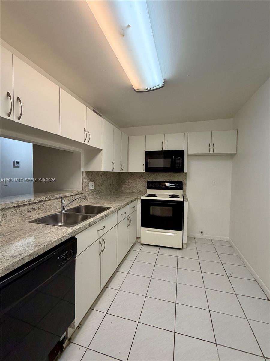 A kitchen features white cabinets, granite countertops, a black stove, and white floor tiles — MIAMI, FL