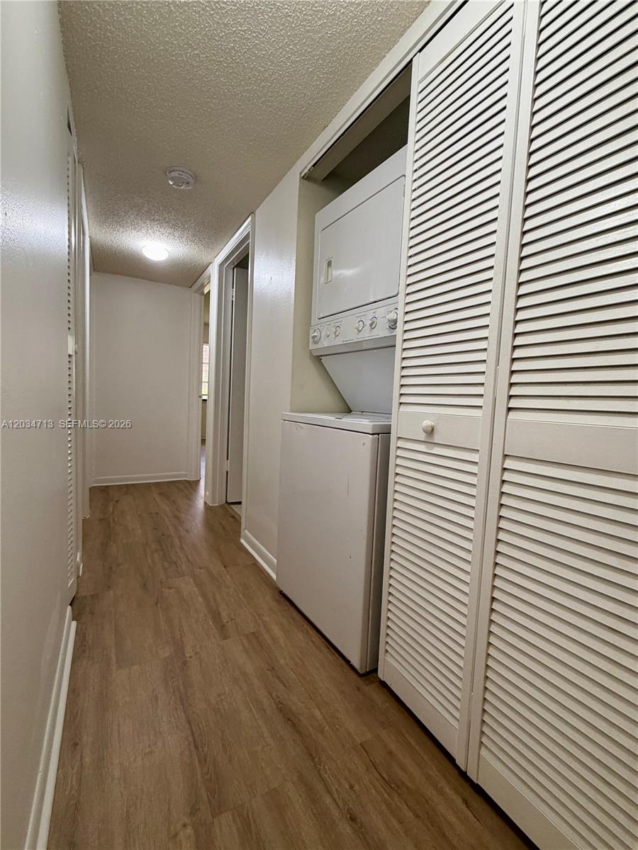 A hallway features wood-look flooring, white walls, and a stacked washer and dryer unit — MIAMI, FL