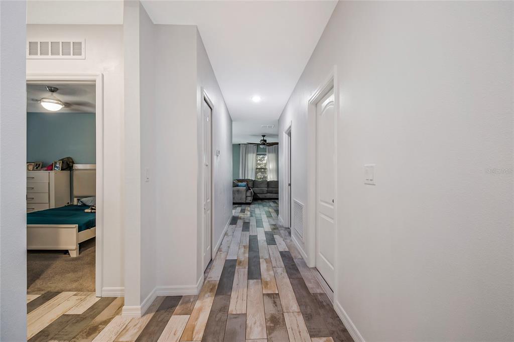 A hallway with wood-look plank flooring leads to a living area with a ceiling fan — 328 HIBISCUS DRIVE, POINCIANA, FL