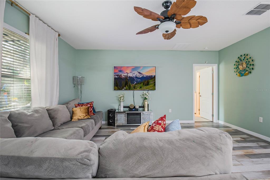 A living room features a gray sectional sofa, a wall-mounted television, and a ceiling fan — 328 HIBISCUS DRIVE, POINCIANA, FL