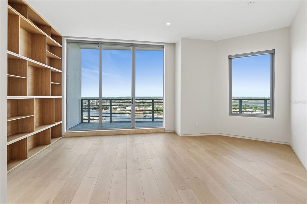 An empty room with light wood flooring, a built-in bookshelf, and floor-to-ceiling windows — 1209 E CUMBERLAND AVENUE UNIT 2902, TAMPA, FL
