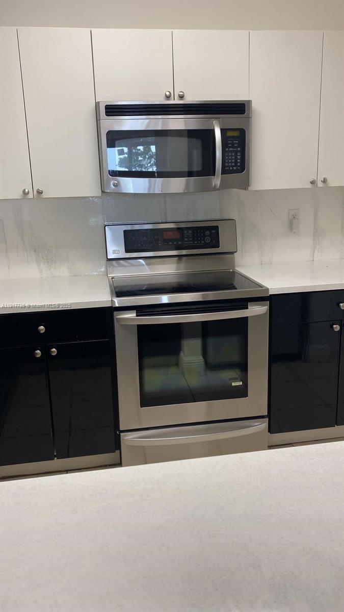 A kitchen features white upper cabinets, black lower cabinets, and stainless steel appliances — 6930 Miami Gardens Dr # 410, Hialeah FL 33015, HIALEAH, FL