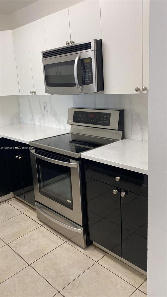 A kitchen features white upper cabinets, black lower cabinets, stainless steel appliances, and tiled floors — 6930 Miami Gardens Dr # 410, Hialeah FL 33015, HIALEAH, FL