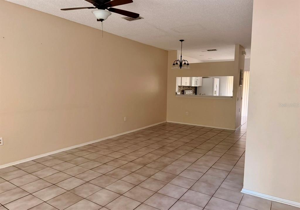 An open living area features tile flooring, a ceiling fan, and a kitchen pass-through window — 29914 ALTA VITA LANE, WESLEY CHAPEL, FL