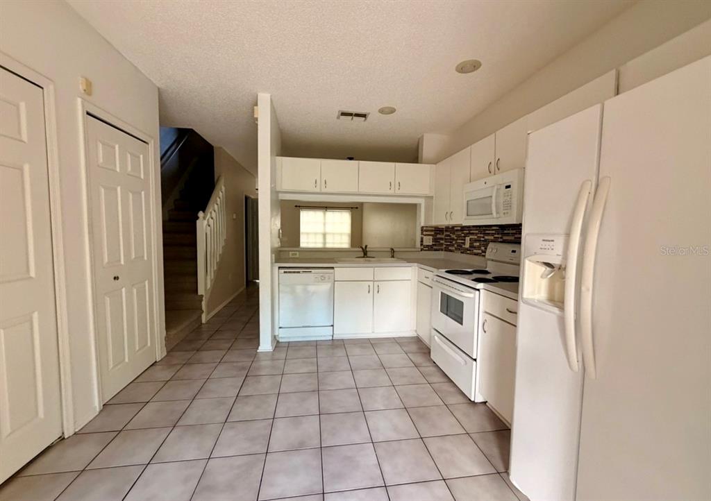 A kitchen with white cabinets, tile flooring, and a staircase leading to an upper level — 29914 ALTA VITA LANE, WESLEY CHAPEL, FL