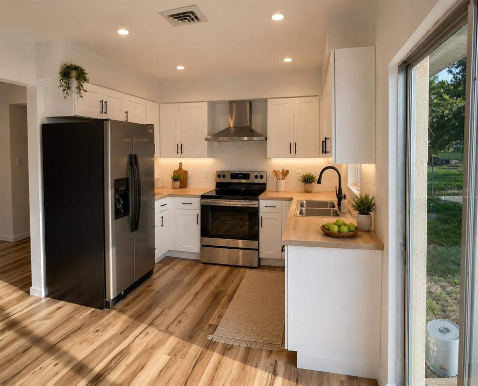 A kitchen with white cabinets, stainless steel appliances, wood countertops, and wood-look flooring — 1051 VENETIAN PARKWAY, VENICE, FL