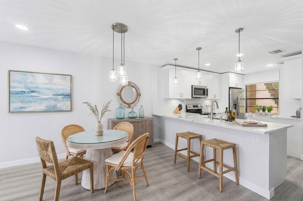 A bright kitchen and dining area features white cabinets, a breakfast bar, and rattan chairs — 21839 Arriba Real # 10g, Boca Raton FL 33433, BOCA RATON, FL