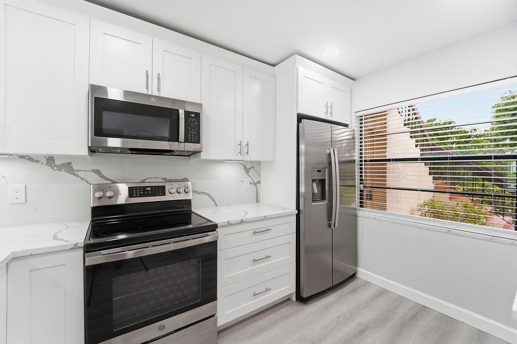 A modern kitchen features white cabinets, stainless steel appliances, and marble-patterned countertops and backsplash — 21839 Arriba Real # 10g, Boca Raton FL 33433, BOCA RATON, FL
