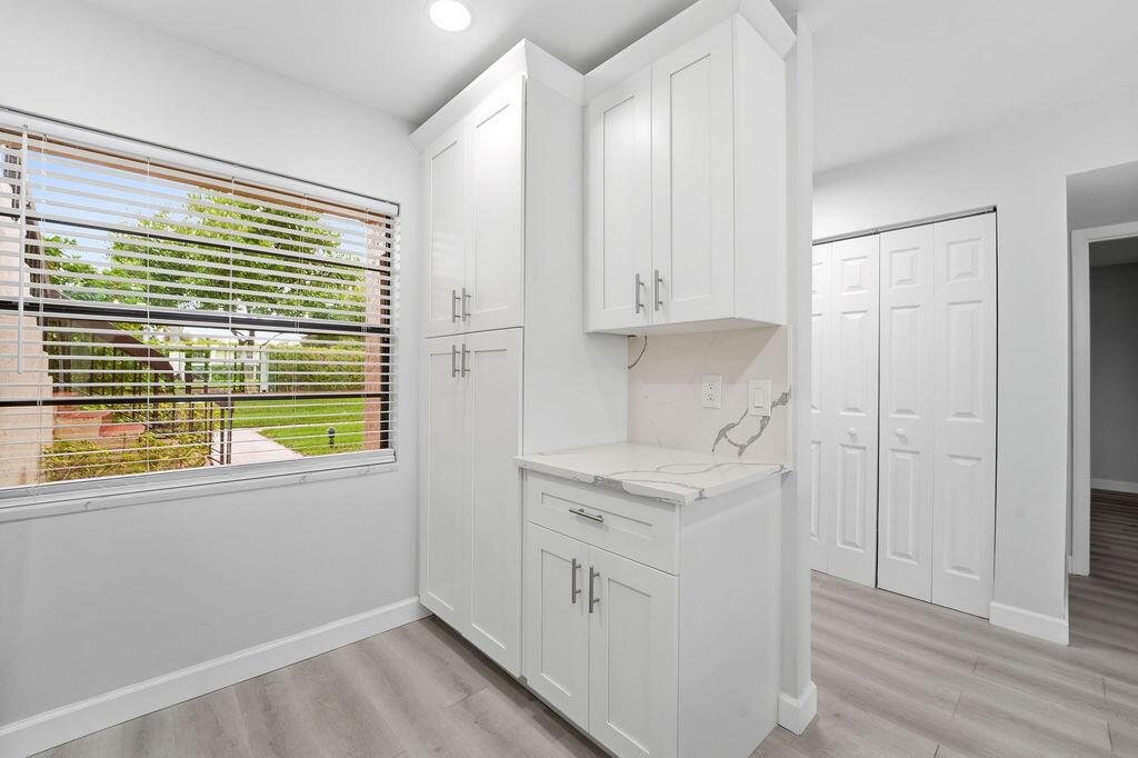 A white kitchen cabinet unit with a marble countertop sits next to a windowed wall — 21839 Arriba Real # 10g, Boca Raton FL 33433, BOCA RATON, FL